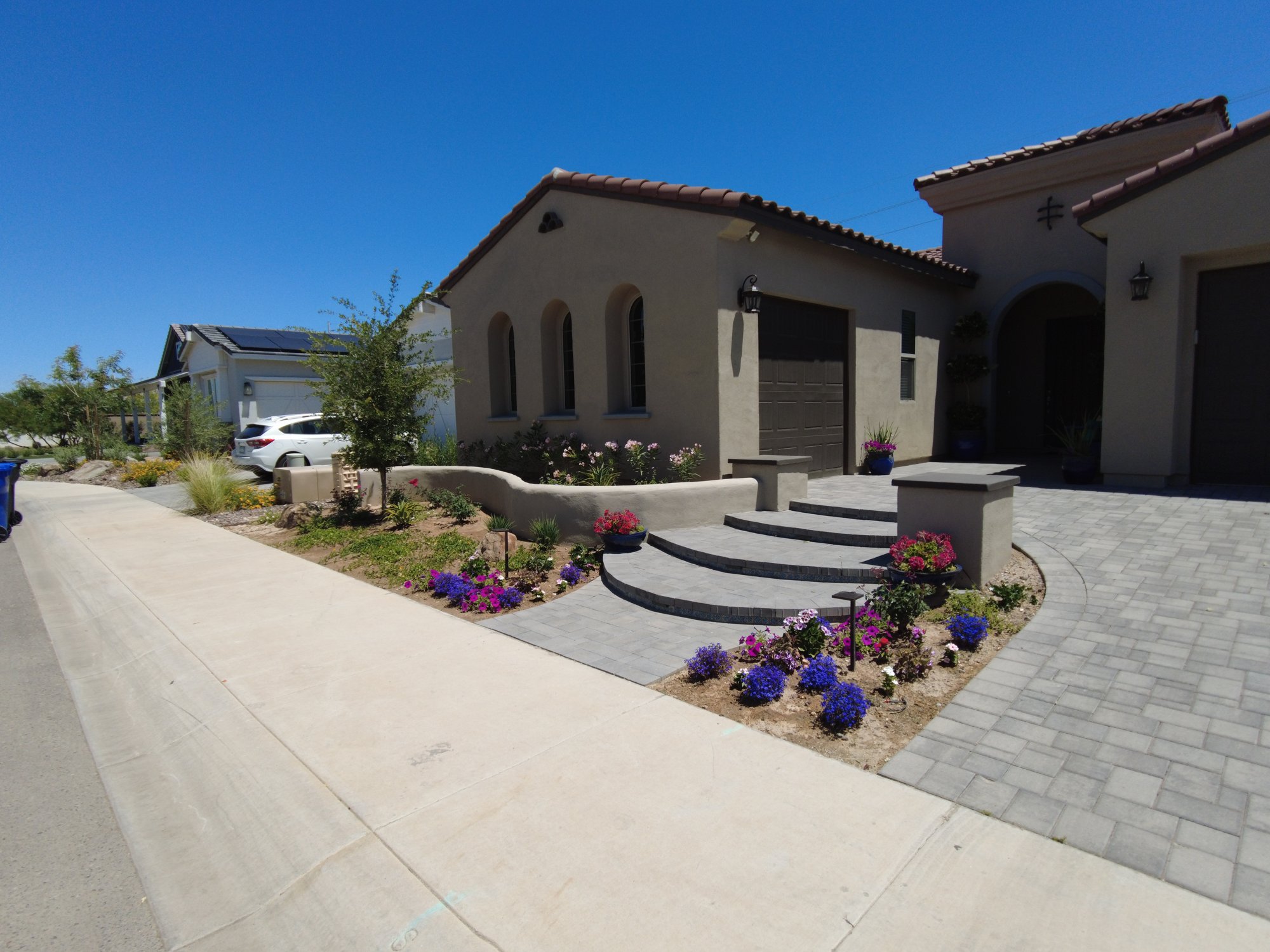 Finished front yard with curved gray paver steps between stucco pillars, a curved stucco seat wall, flower beds with landscape lights and the paver driveway.