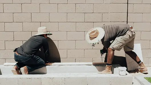 Two hardscape installers working alongside a block wall