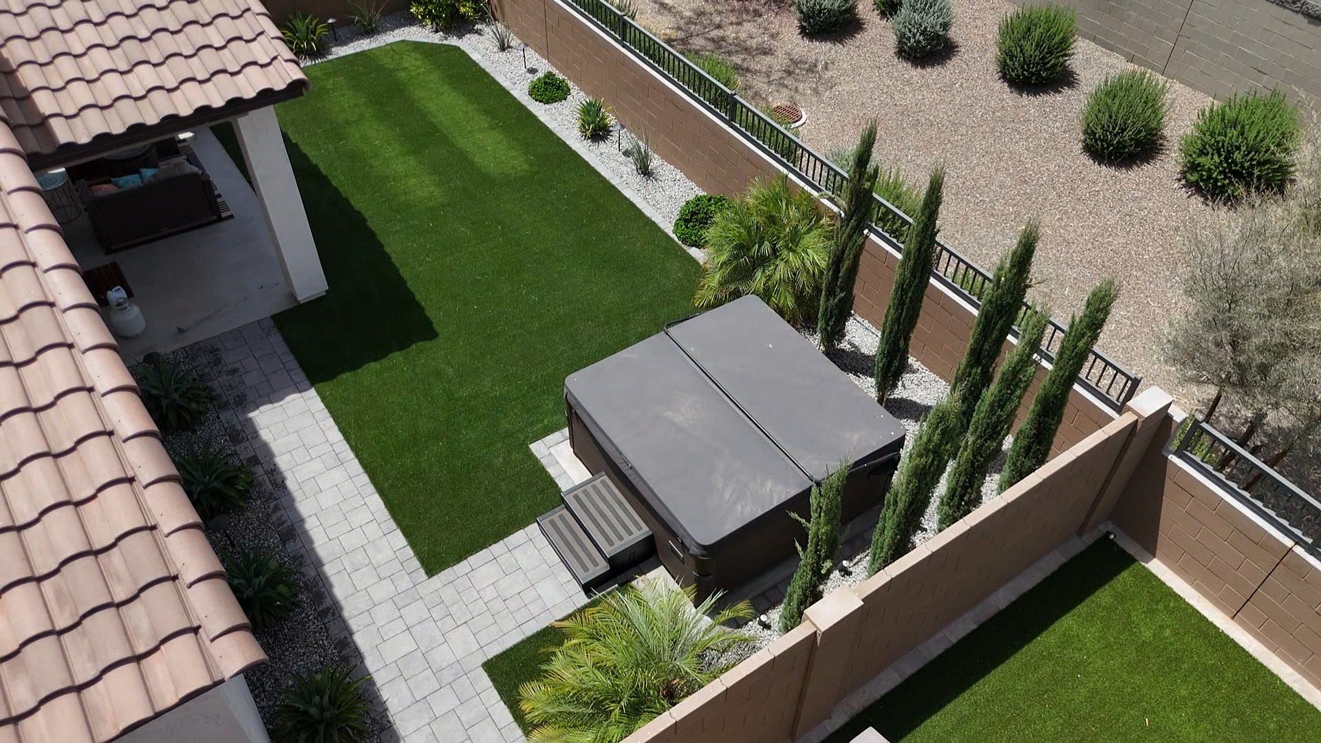 Aerial view of the finished backyard with striped artificial turf, a paver walkway, desert landscaping and a hot tub.