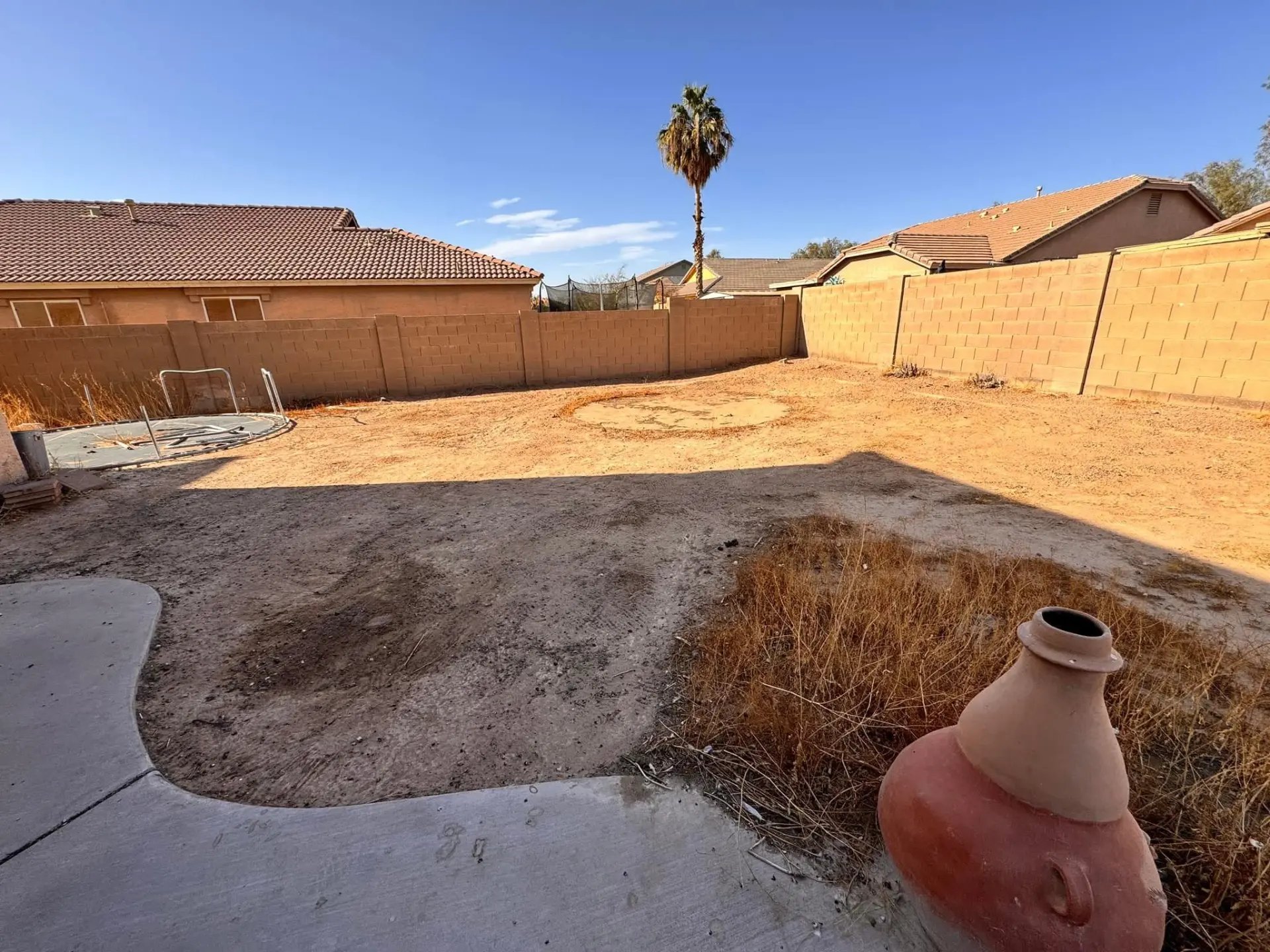 Backyard of bare dirt with dead brush, a dismantled trampoline frame and a clay chiminea, before the yard was rebuilt.