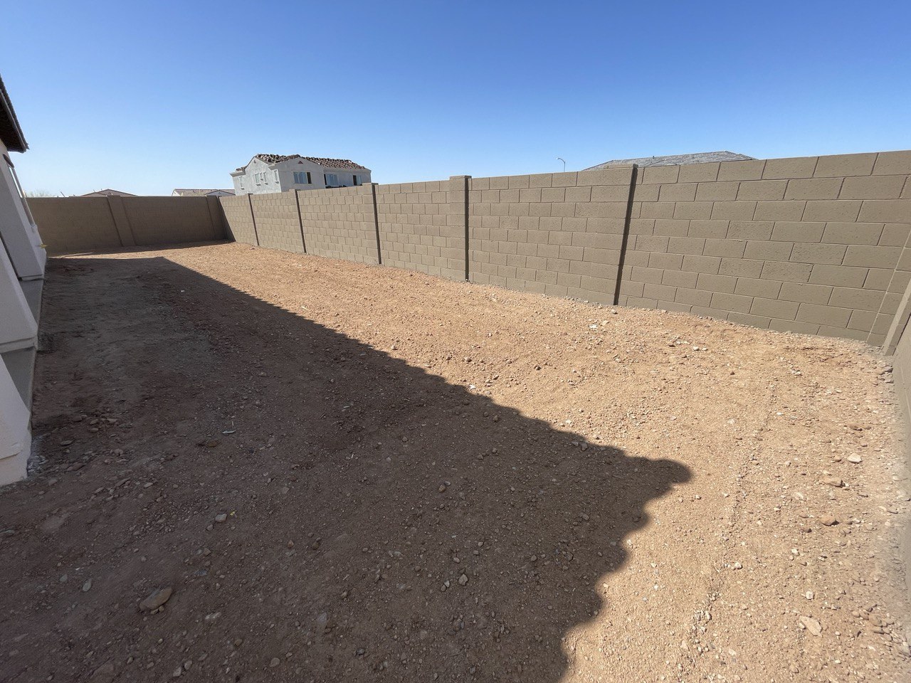 Long new construction backyard of bare dirt inside tan block walls, before any landscaping.