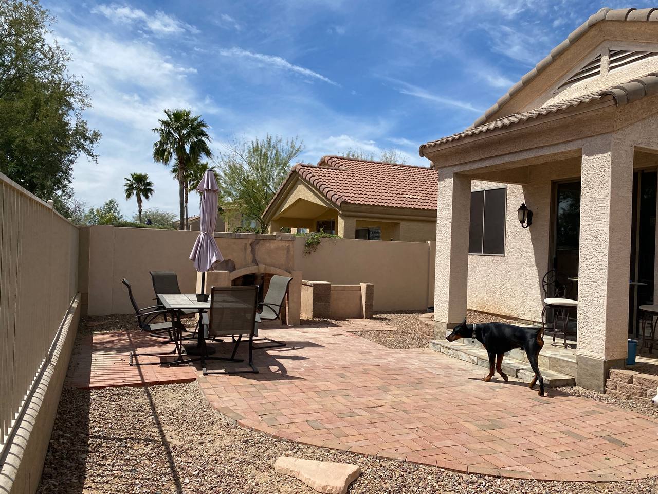 Side yard with an old worn brick paver patio, gravel and a block fire feature beside a covered patio, before the remodel.