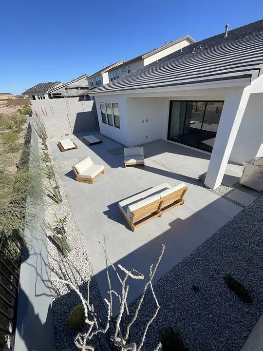 Modern patio with white walls, cushioned wooden seating, and desert landscaping under a clear blue sky.