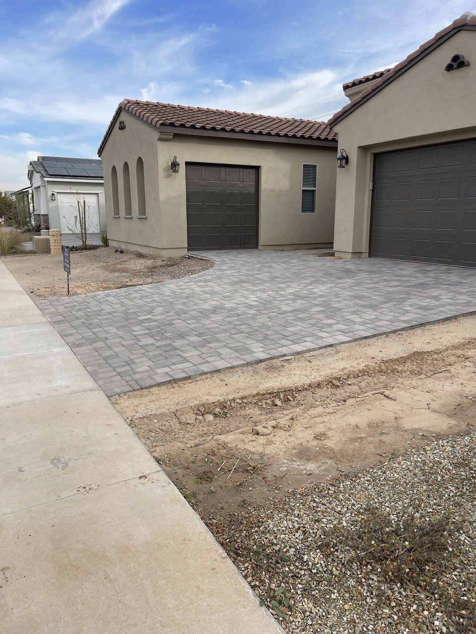Front of a stucco home with a new gray paver driveway beside bare dirt and gravel along the sidewalk, before the front yard was finished.