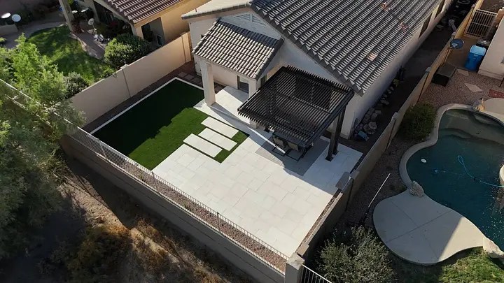 Aerial view of a backyard with a pool, patio, pergola, and artificial turf lawn.