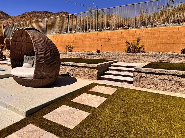 Outdoor patio with a wicker lounger, stone steps, and desert landscaping under a clear blue sky.